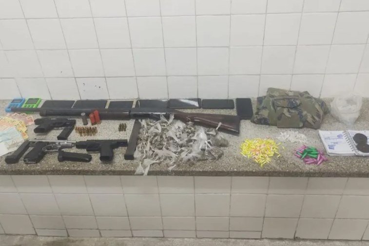 Foto colorida de bancada com armas, drogas e dinheiro apreendido pela polícia - Metrópoles