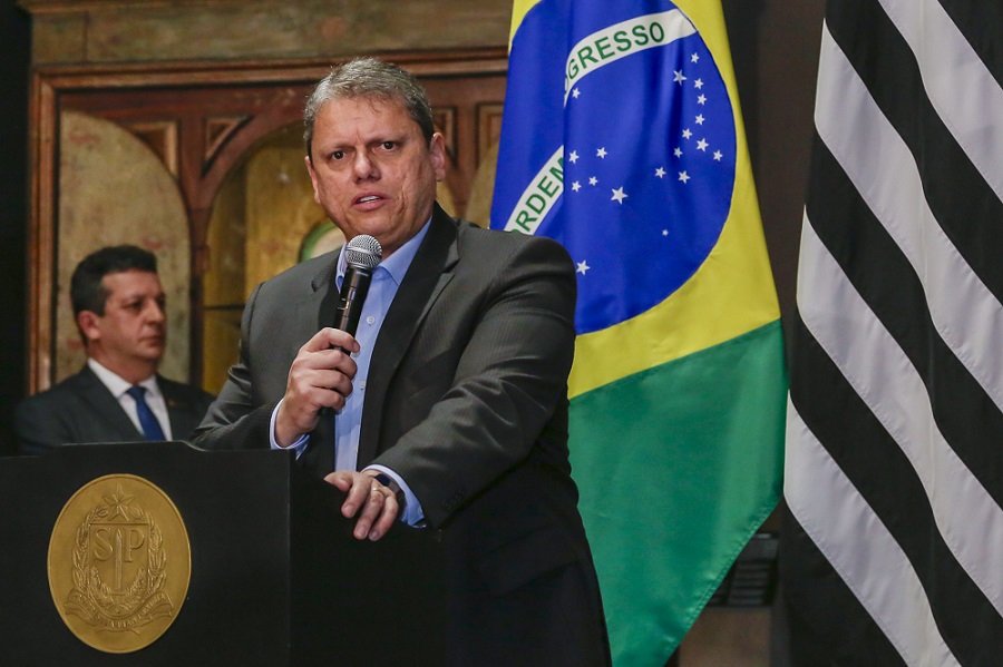 Fotografia colorida do governador Tarcísio de Freitas discursando em pé e segurando o microfone com a mão direita. Ao fundo, as bandeiras do Brasil e de São Paulo - Metrópoles