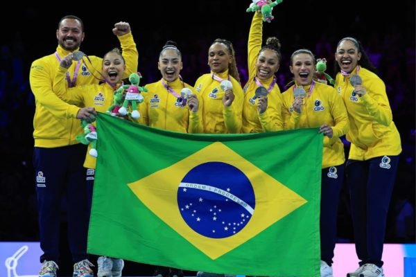 Imagem mostra time feminino de ginástica artística do Brasil posando com bandeira do Brasil- Metrópoles
