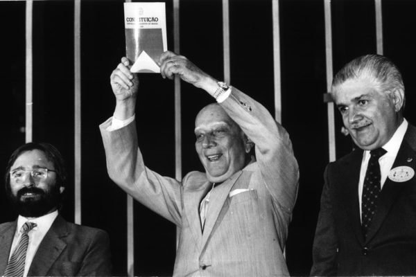 Imagem em preto e branco de Ulysses Guimarães com a Constituição de 1988 - Metrópoles