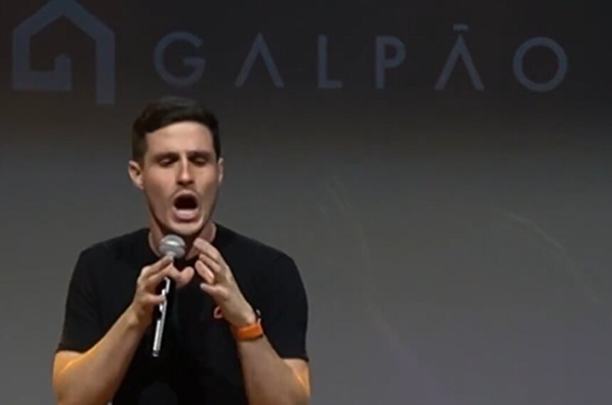 Em foto colorida homem branco de camiseta preta fala do microfone - Metrópoles