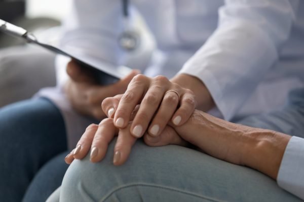Foto mostra médica dando a mão para uma paciente