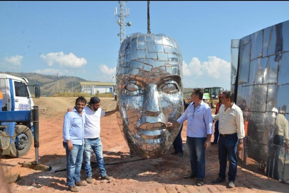 Foto colorida de homens ao redor de rosto esculpido com aço - Metrópoles