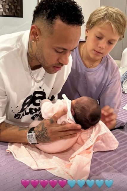 Foto colorida de um bebê no colo e um adulto - Metrópoles