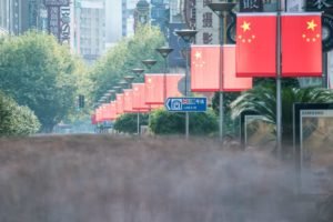 Imagem de rua na China, com várias bandeiras do país e prédios ao fundo - Metrópoles