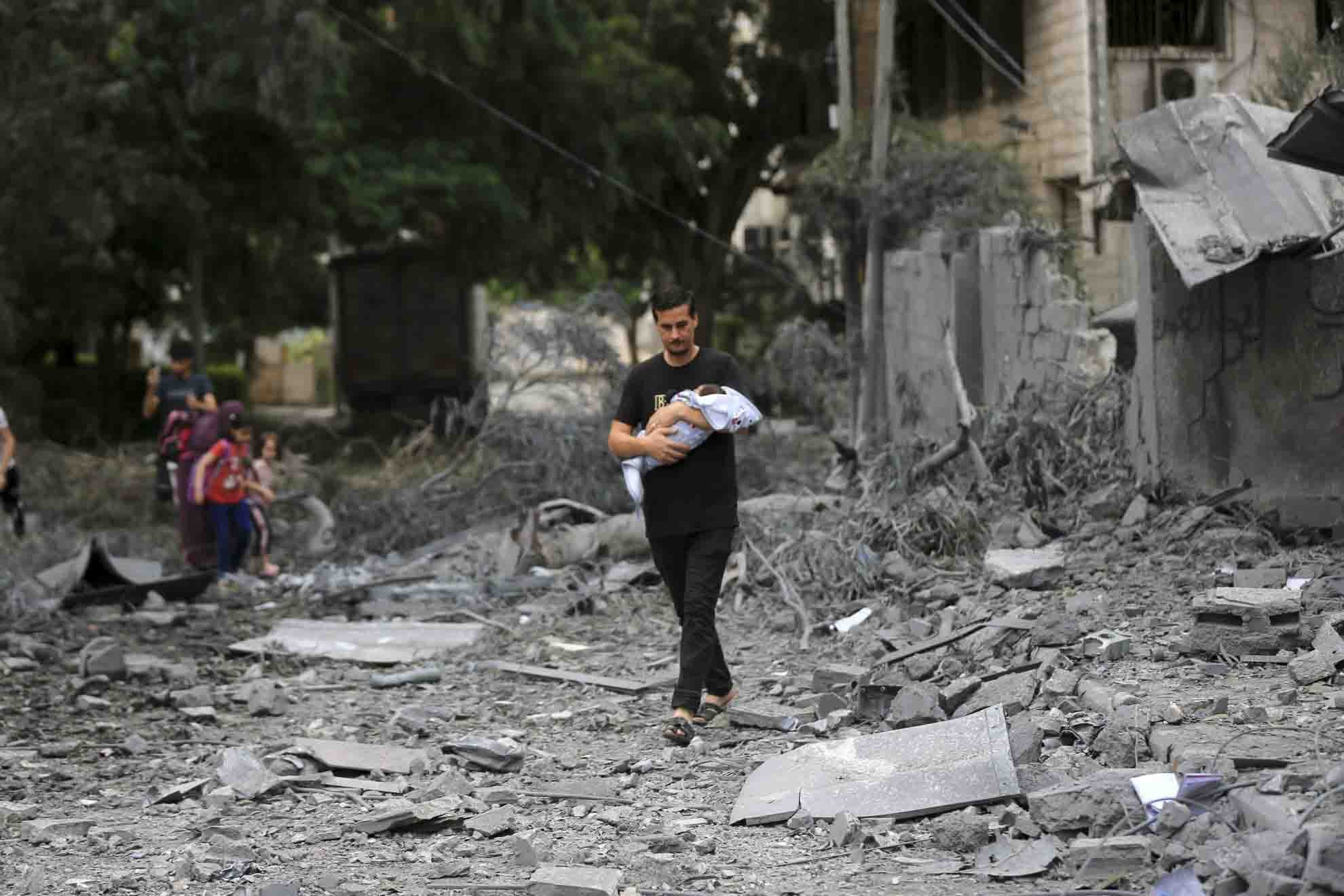 Homem com criança de colo se muda para um local mais seguros em meio a edifícios destruídos e destroços após ataques aéreos - metrópoles