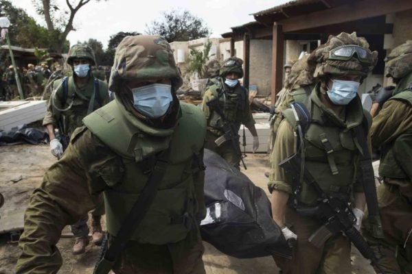 Soldados israelenses removem os corpos de civis, que foram mortos dias antes em um ataque de militantes palestinos neste kibutz perto da fronteira com Gaza - Metrópoles