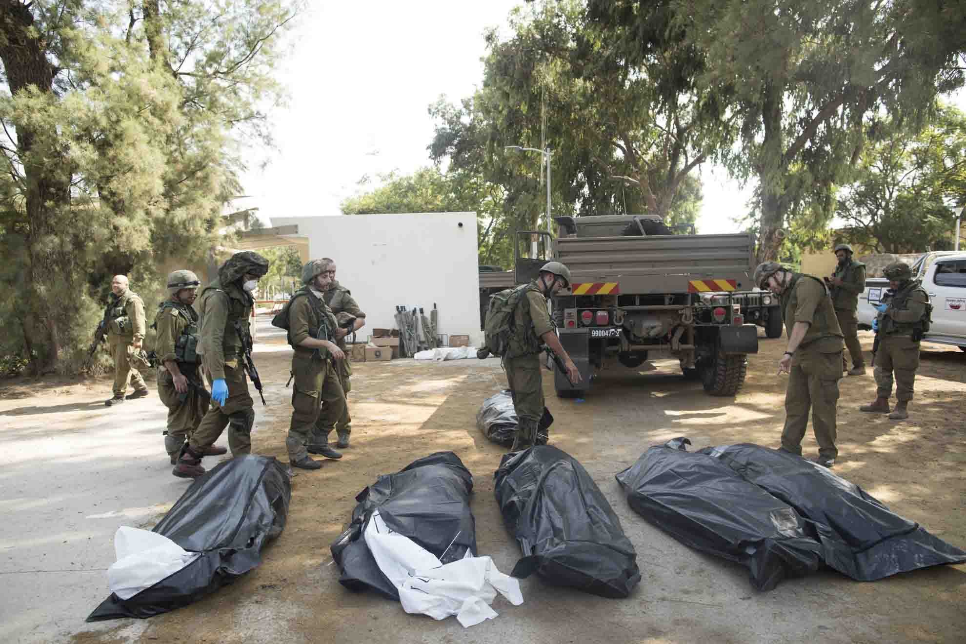 Soldados israelenses removem os corpos de civis, que foram mortos dias antes em um ataque de militantes palestinos neste kibutz perto da fronteira com Gaza - Metrópoles