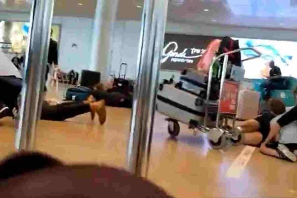 Imagem colorida de pessoas deitas no chão em aeroporto após ataque - Metrópoles