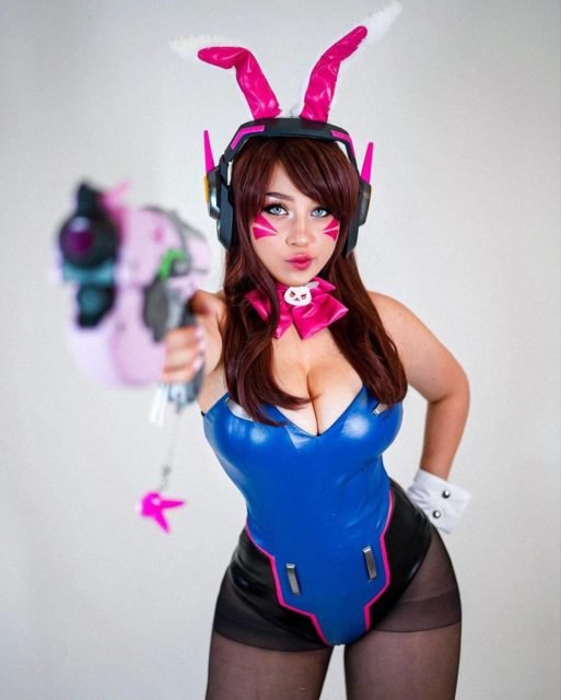 foto colorida de mulher de meia calça preta, maio azul e orelhas rosas de coelho segurando arma rosa - metrópoles