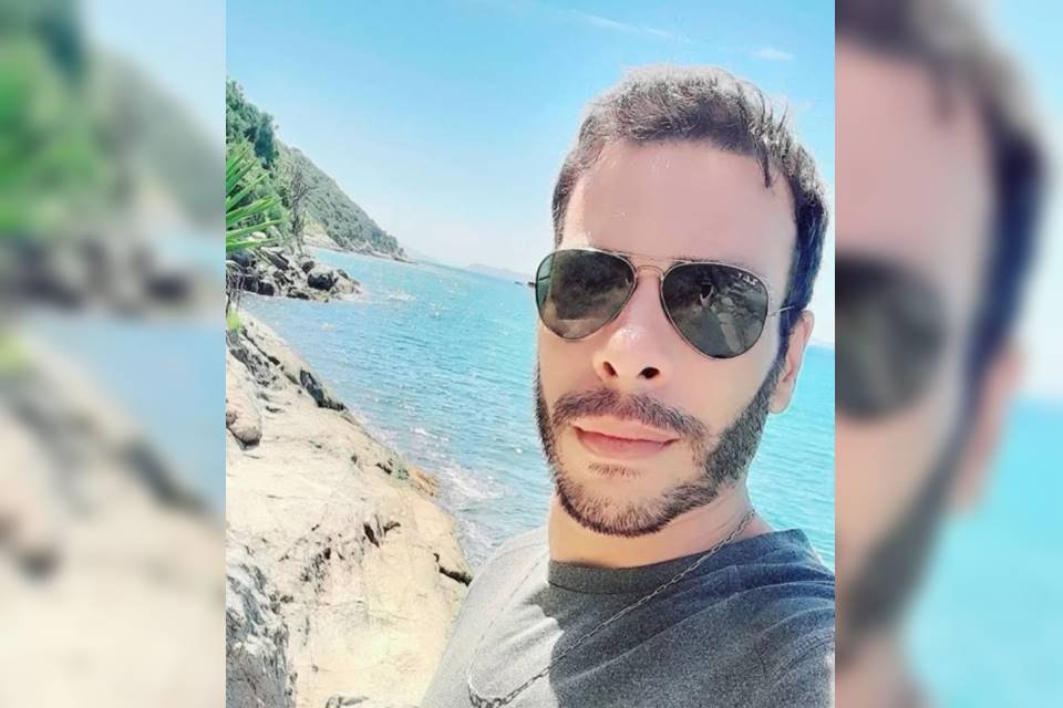 Homem com ósculos escuros e camiseta preta com mar ao fundo - Metrópoles