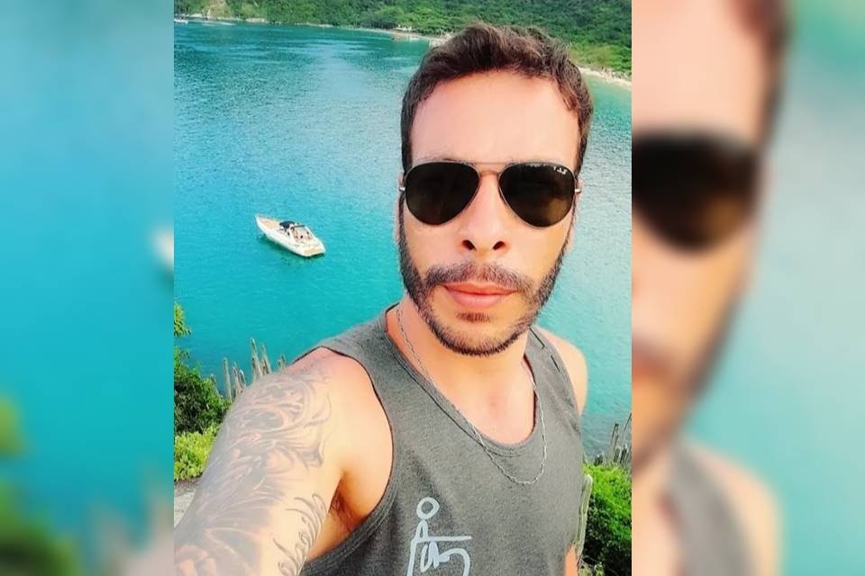 Homem de óculos escuros e regata tira selfie com o mar ao fundo - Metrópoles