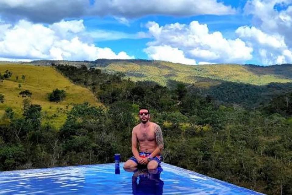 Homem dentro de piscina com mata fechada ao fundo e céu com nuvens - Metrópoles