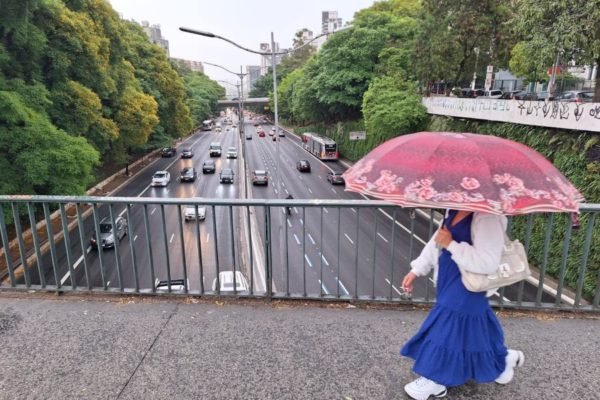 Imagem mostra mulher com saia azul, camisa clara e guarda-chuva rosa caminhando sobre viaduto - Metrópoles