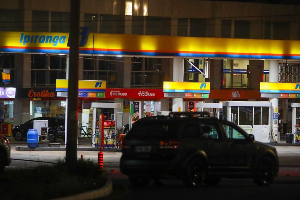 Imagem colorida de carro da PMDF, em área externa, à noite, próximo a posto de combustível Ipiranga, ao fundo