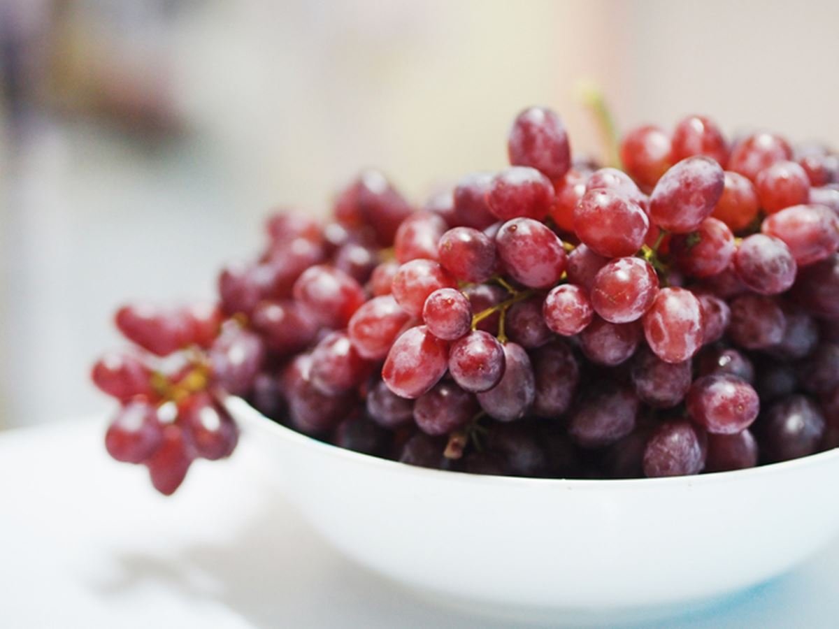 Foto colorida de pote branco com uvas roxas - Metrópoles