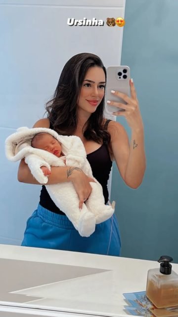 Foto colorida de Bruna Biancardi e Mavie. Uma mulher branca, com cabelo preto, segura a filha no colo e tira uma foto com o celular na outra mão - Metrópoles