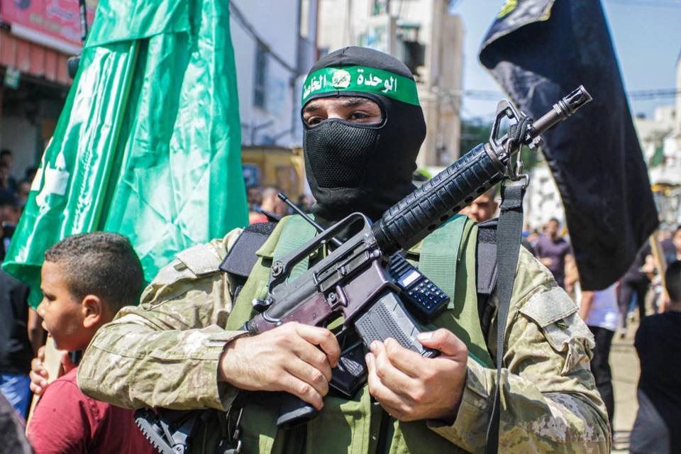 Imagem colorida mostra um membro do Hamas segurando um rifle durante um funeral na Palestina - Metrópoles