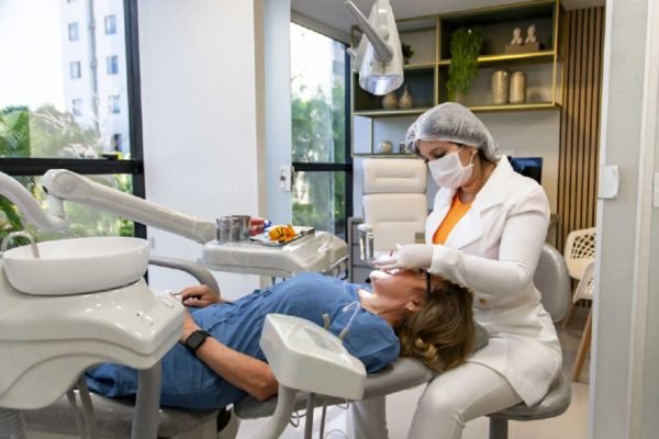 foto colorida de uma mulher deitada em uma cadeira de dentista enquanto uma profissional faz o atendimento - Metrópoles