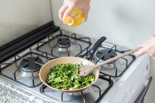 Imagem colorida de pessoa cozinhando folhas em frigideira - Metrópoles