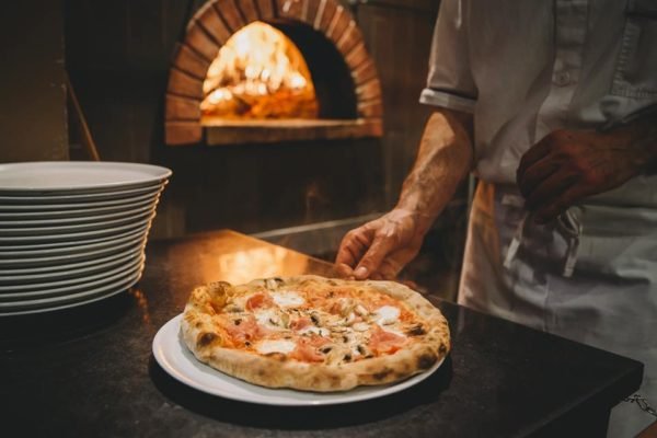 Foto colorida de um restaurante e uma pizza - Metrópoles