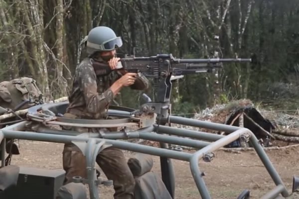 Em foto colorida, militar do exército aponta com metralhadora de grosso calibre instalada sobre um jipe militar - Metrópoles