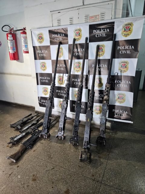 Fotografia colorida mostra metralhadoras enfileiradas em frente a um painel da Polícia Civil de São Paulo - Metrópoles