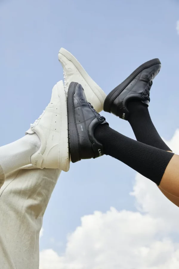 Na imagem com cor, duas pernas levantadas com tênis preto e branco juntos - Metrópoles