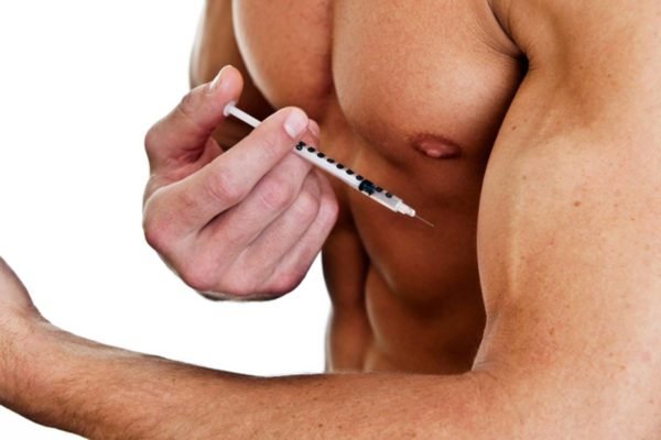 Imagem colorida de pessoa musculosa aplicando injeção de esteróide no músculo - Metrópoles