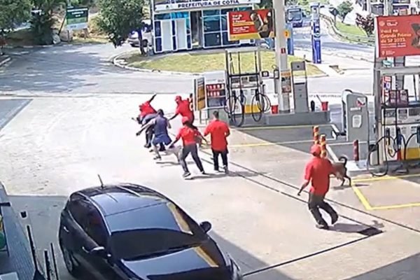 Imagem colorida mostra grupo de frentistas vestidos de vermelho em volta de um homem com capacete vestido de preto; bandido tentou assaltar um posto de gasolina em Cotia e acabou apanhando - Metrópoles