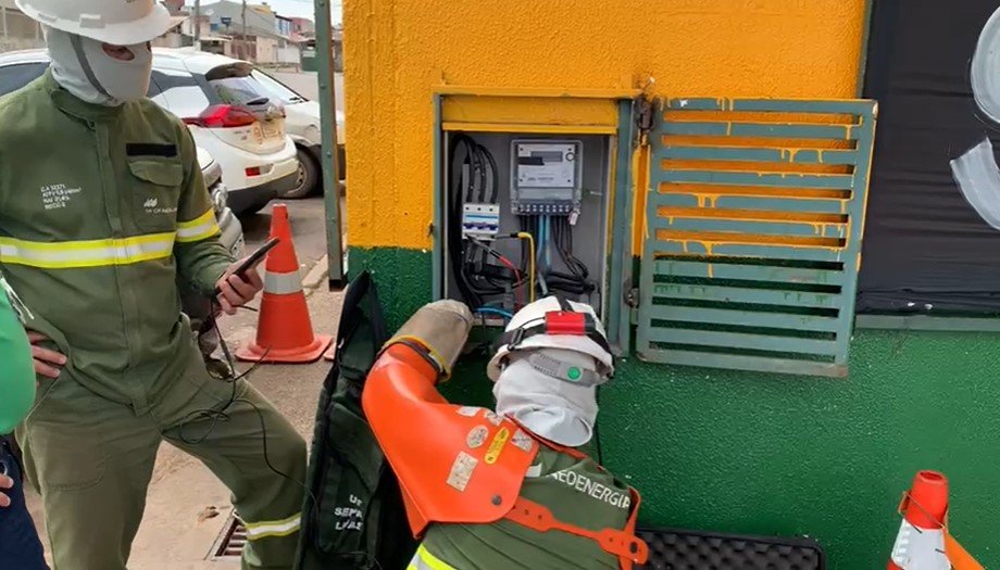 Imagem colorida de pessoas com uniforme da Neoenergia verificando relógio de energia - metrópoles