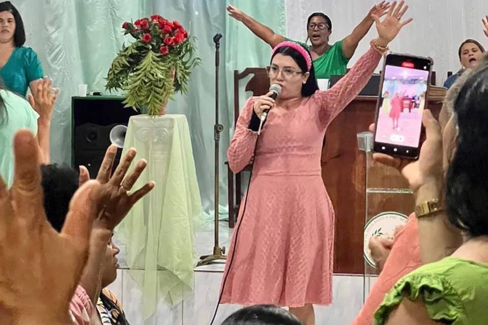 Foto colorida de Sara Mariano cantando em microfone em igreja - Metrópoles