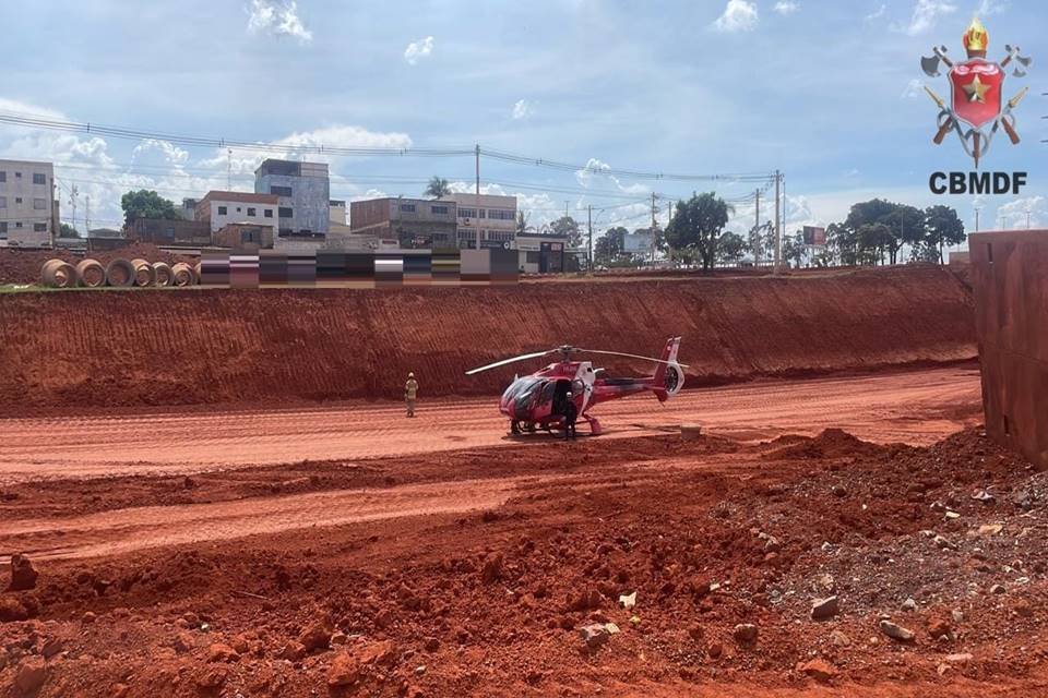 Foto colorida de terreno amplo com terra vermelha e helicóptero do corpo de bombeiros no local