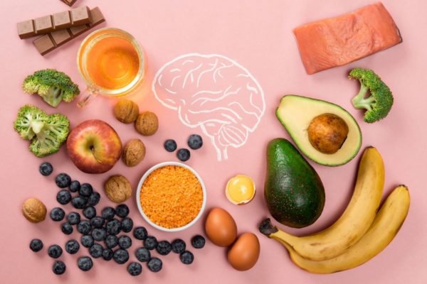 Foto colorida de cérebro desenhado e rodeado de alimentos, como maçã, ovo, uva, cúrcuma, abacate, salmão e banana - Metrópoles