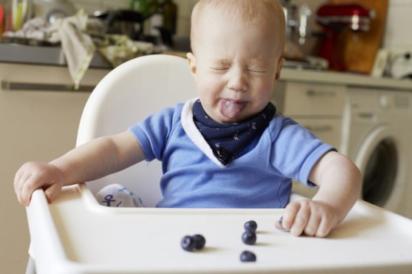 Foto de estoque de Bebê mostrando a língua para mirtilos na cadeira alta
