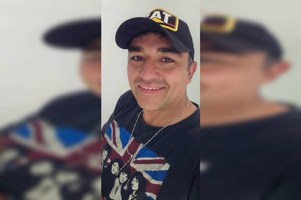 Foto colorida de homem branco com boné e blusa azul