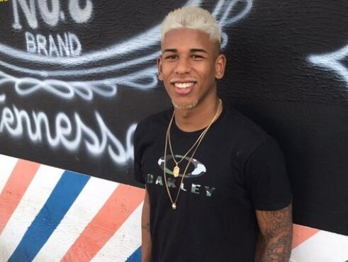 Foto colorida mostra Felipe Diogo com cabelo descolorido, camiseta preta, e correntes douradas