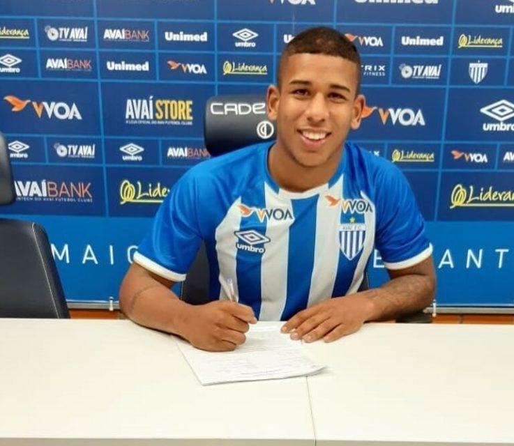 Foto colorida mostra Felipe Diogo assinando contrato, com uniforme do Avaí