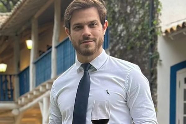 Felipe Becari posa de camisa social, gravata e uma taça de vinho na mão - Metrópoles