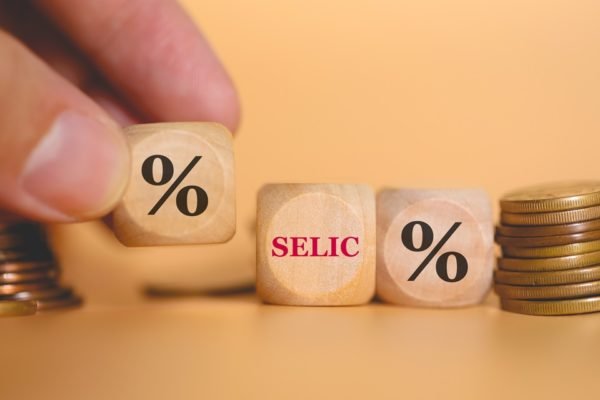 Imagem de uma mão mexendo com dados em que aparecem símbolos de porcentagem e o nome "Selic", em alusão à taxa de juros - Metrópoles