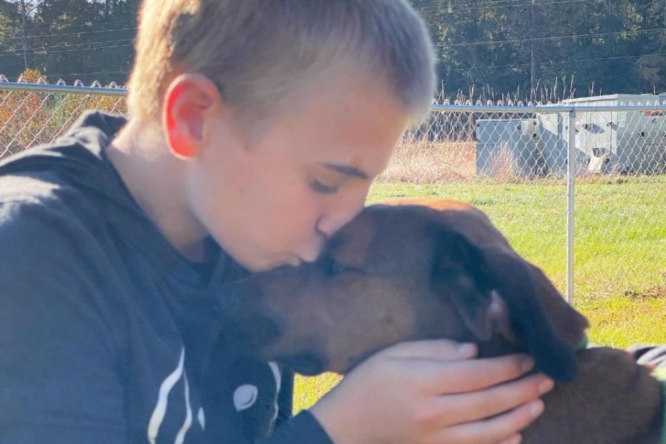 Foto colorida de um menino beijando um cachorro - Metrópoles
