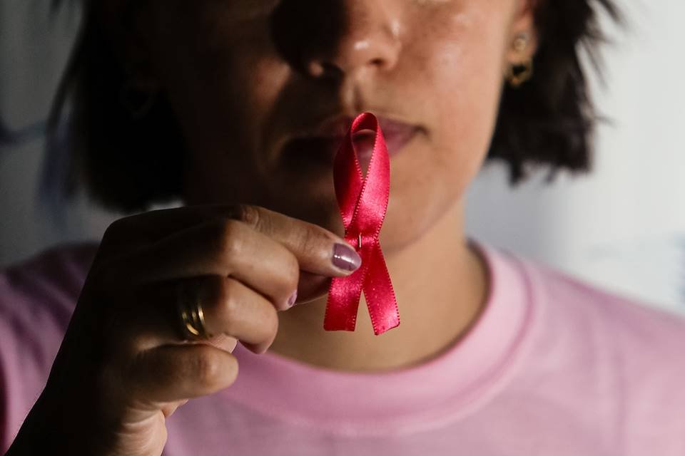 Foto colorida com mulher branca segurando símbolo rosa