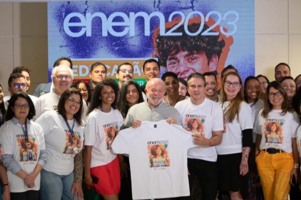 Imagem colorida mostra o presidente Lula segurando uma camiseta branca cercado por várias pessoas que também vestem uma camiseta branca na sede do Inep - Metrópoles