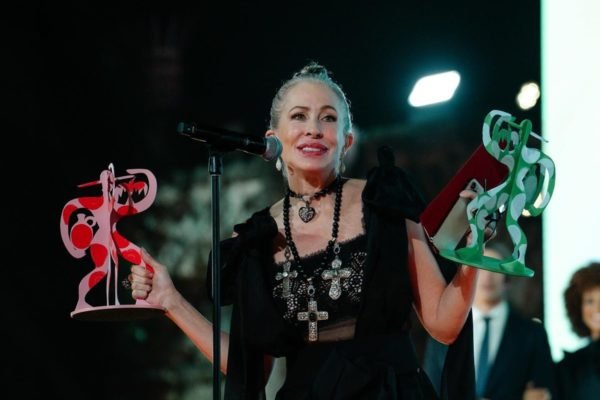 Em palco de premiação, mulher segura dois troféus coloridos - Metrópoles