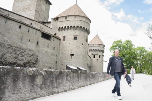 Foto colorida de homem caminhando ao lado de castelo - Metrópoles