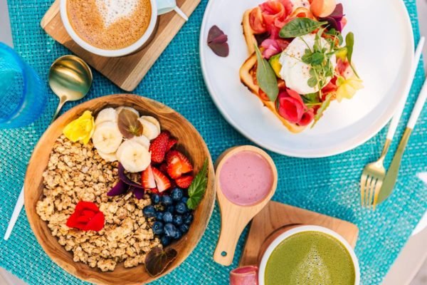 Foto colorida de mesa com bowls de frutas e vitaminas; prato com torrada; e xícara de café - Metrópoles