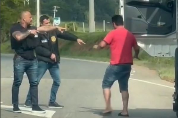 Em foto colorida dois policiais abordam homem com camiseta vermelha e bermuda jeans - Metrópoles