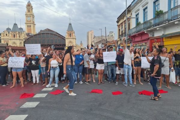 Imagem colorida mostra pessoas segurando cartazes em frente a Estação da Luz, na região da Cracolândia; elas protestam contra a ida do fluxo de usuários para a rua Mauá
