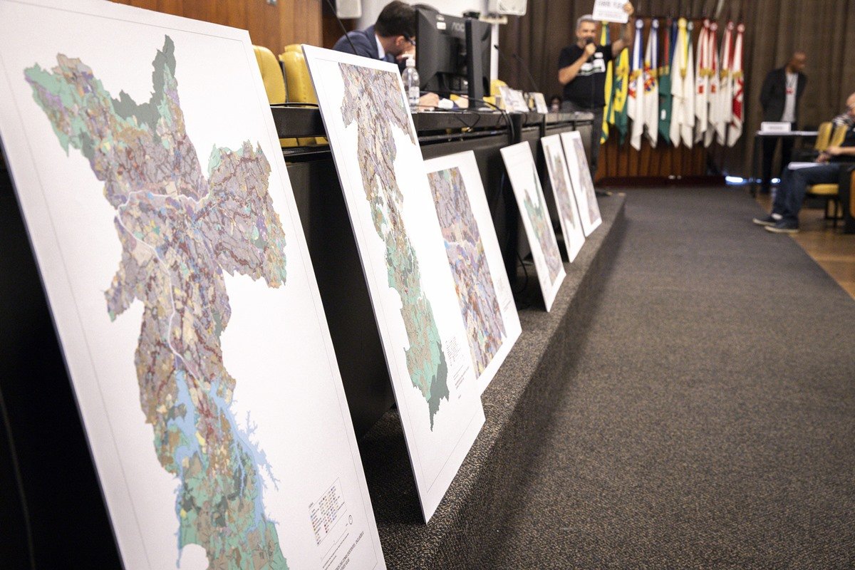 Imagem colorida mostra auditório da Câmara Municipal com série de mapas da cidade fixados no palco - Metrópoles