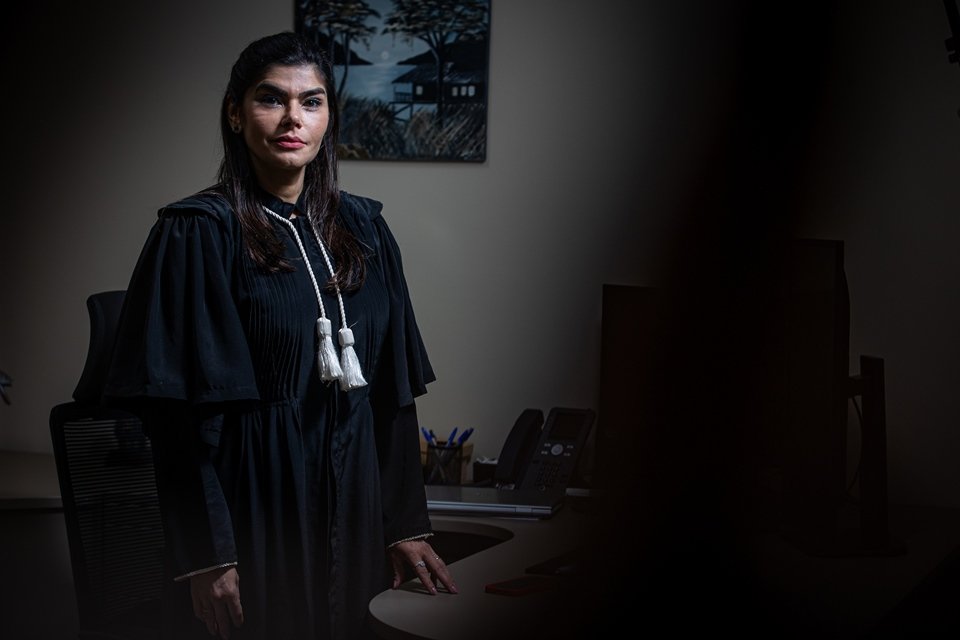 Foto colorida de mulher branca, de cabelos escuros e lisos, vestida com toga de juíza